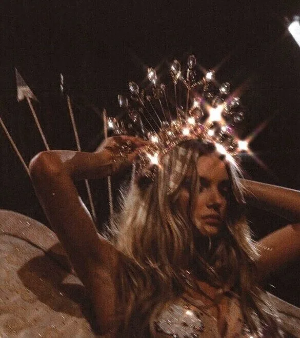 Mujer con una corona de joyas resplandecientes, en iluminación dramática.