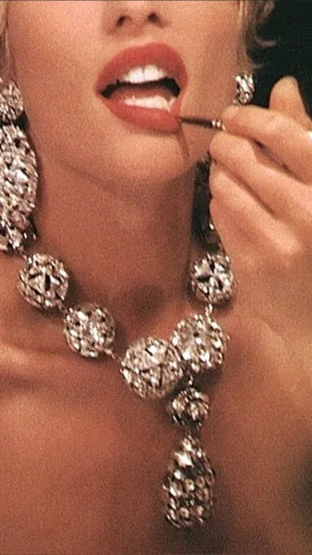 Primer plano de unos labios aplicando labial rojo, con un collar statement de diamantes.