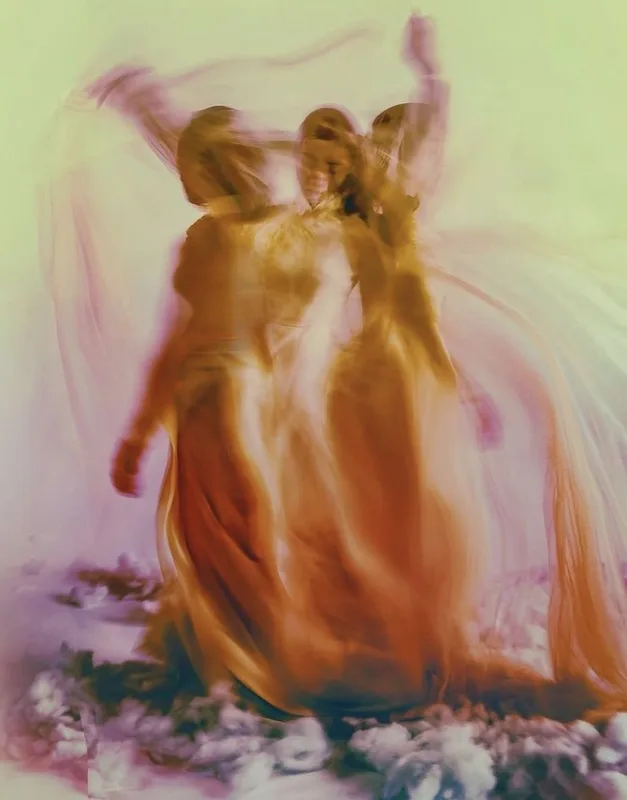 Figuras en movimiento con vestidos vaporosos dorados entre pétalos, en un desenfoque onírico.
